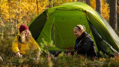 Partiolaisia istumassa metsässä teltan edessä