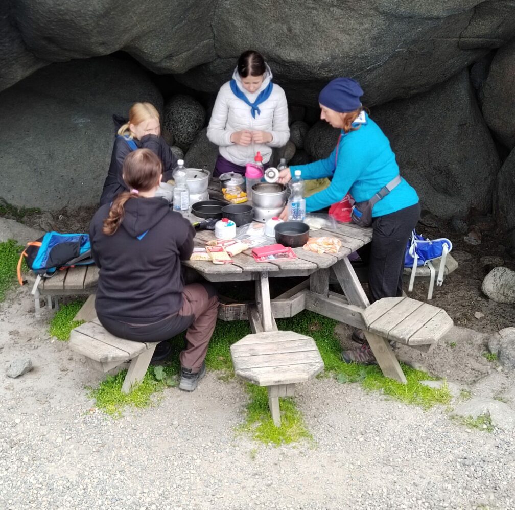Partiolaisia tekemässä ruokaa trangialla pöydän päällä.